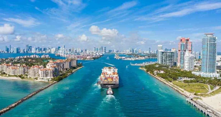 Großes Containerschiff bei der Einfahrt in den Hafen und die Stadt Miami an einem sonnigen Tag, USA. Luftaufnahme.