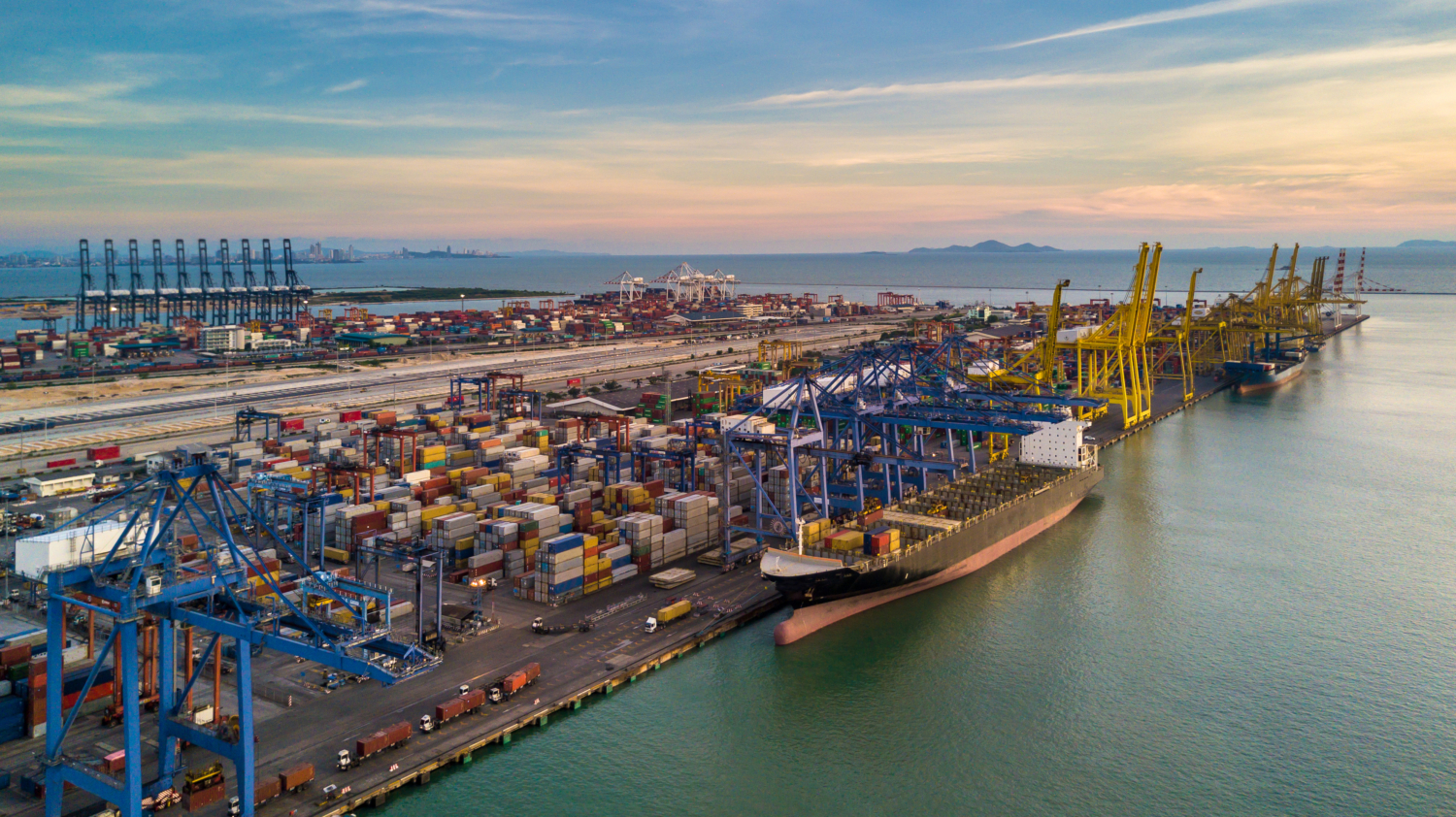Großes Frachtschiff im Containerhafen, umgeben von Kränen und Containern.