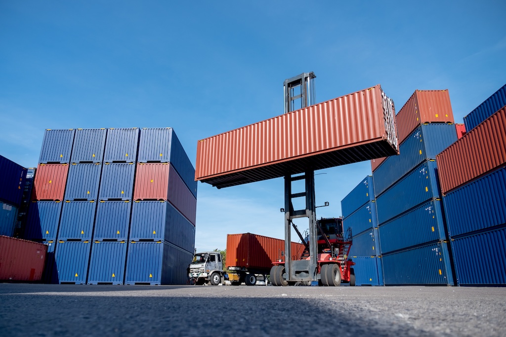 Wide shot of crane truck level up cargo container tank also show stack or layer of containers with different color, blue and brown with carrier truck as back of crane, logistic and delivery concept. Container Abholung Dörrenhaus